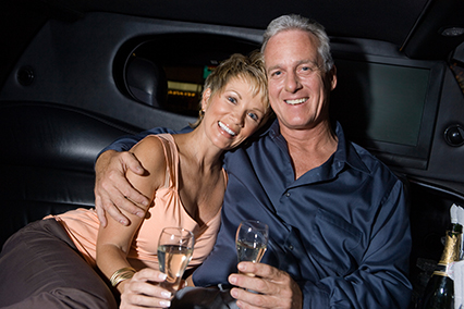 Middle-aged couple sitting on back seat of limousine and drinking champagne, portrait