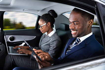 Two Happy African Businesspeople Using Electronic Devices While Traveling By Car