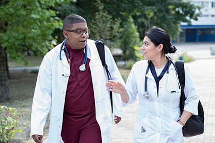 Portrait of walking young interns. Young people, in surgical suits, white coats, with backpacks, with stethoscopes, mixed race. Black guy and mexican girl