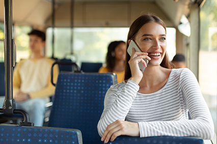 Smiling excited lady taking bus, talking on cellphone