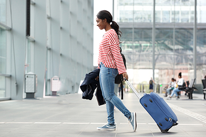 Full length side portrait of young black woman walking with suitcase in airport