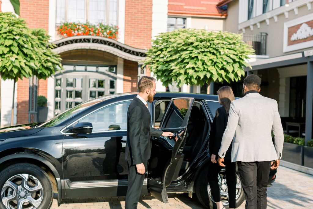 Golden Limo chauffeur opening black SUV car door for business couple head to DTW.