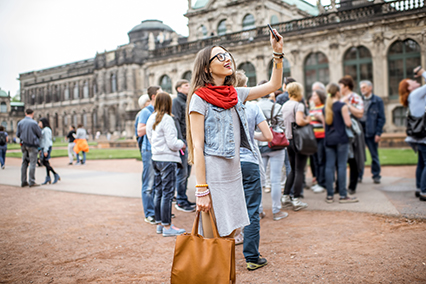 Young smiling woman photographing with smartphone while visiting with tourist group the old palace in Dresden city, Germany
