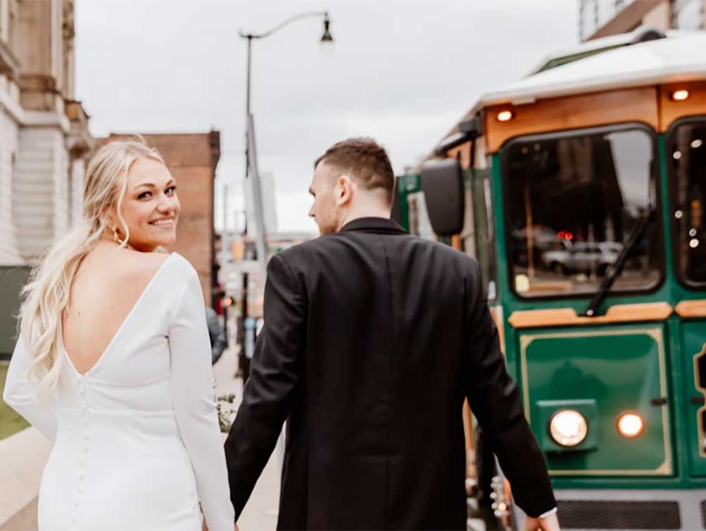 Wedding day bride and groom walking towards Golden Limo Trolley