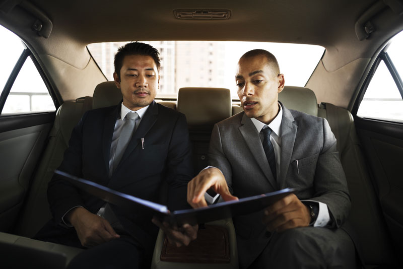 Two businessmen reviewing documents in the back seat of a Golden Limo sedan