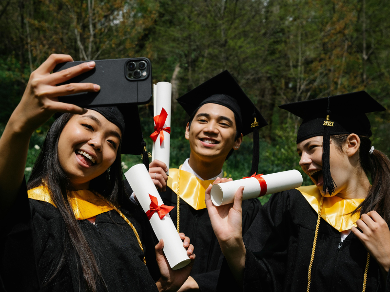 2025_4_GLI_Group-Graudation.png Three college graduates holding degrees and taking a selfie.