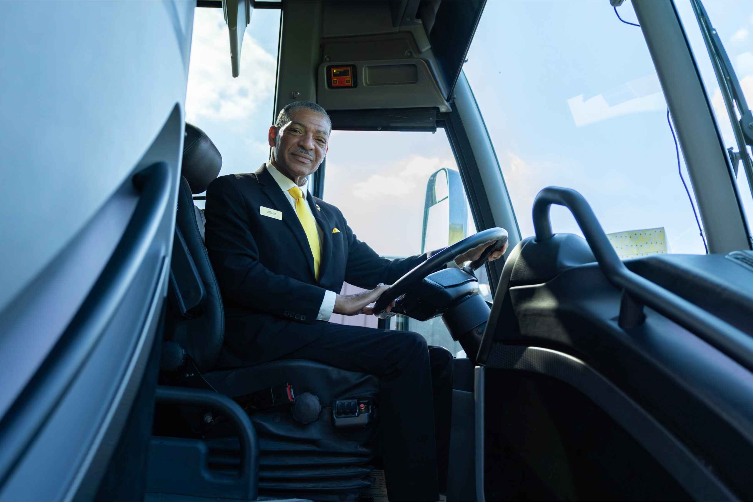 Professional Golden Limousine International motorcoach driver seated behind the wheel of a luxury charter bus, smiling and ready for service.