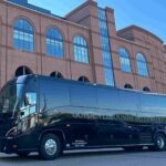 Black luxury motorcoach parked outside a basketball arena, providing group transportation for fans traveling to a major college basketball championship event.