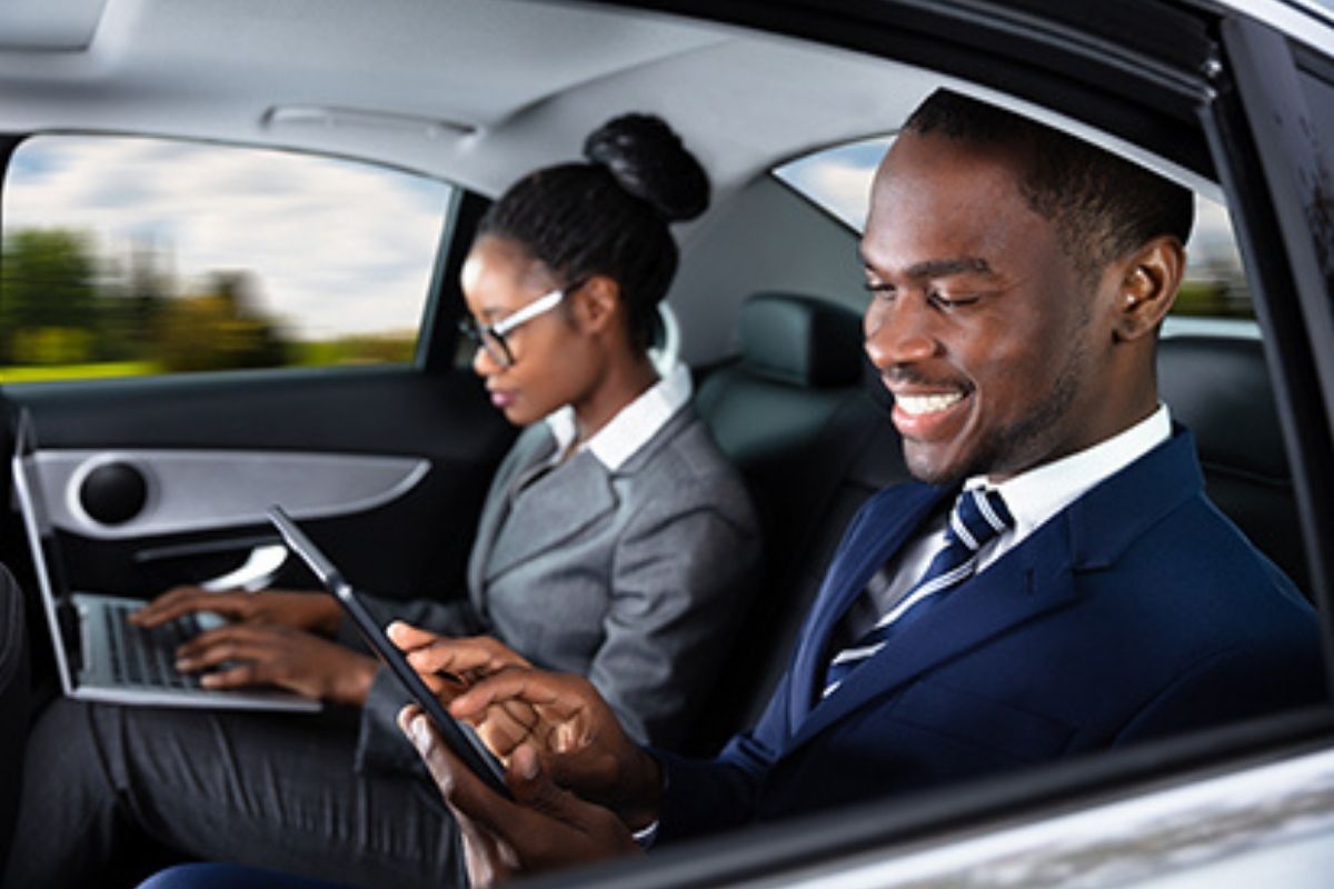 Two business professionals working on laptops and tablets in the back of a Golden Limo sedan.